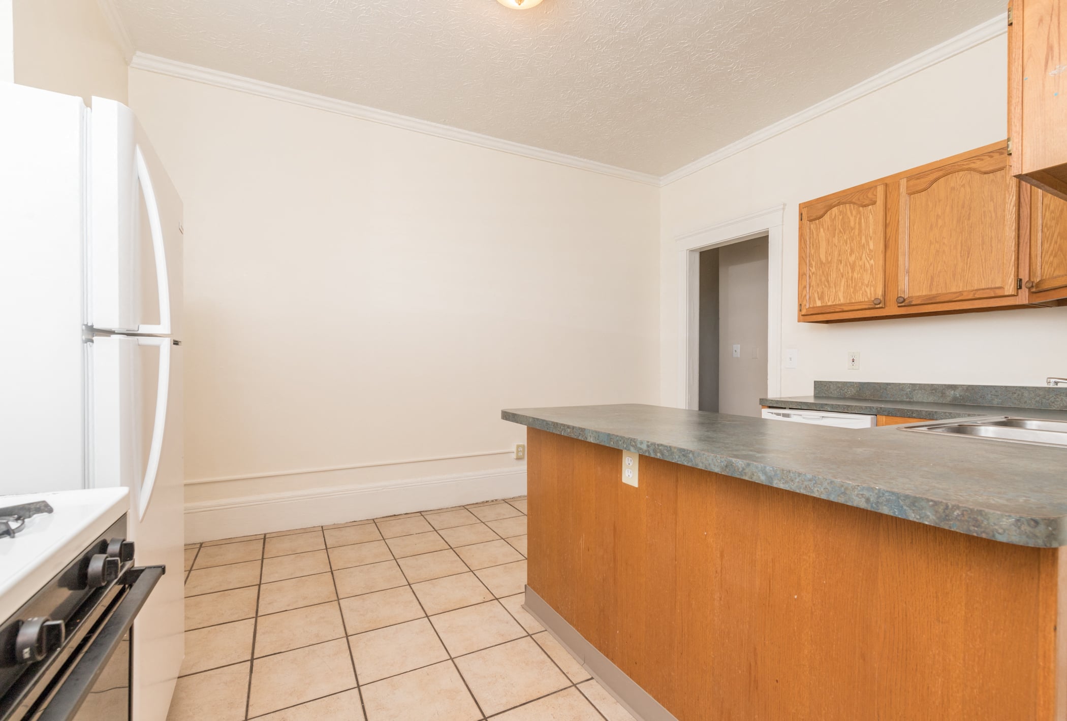 A kitchen with a white fridge, wooden cabinets, and a tiled floor.